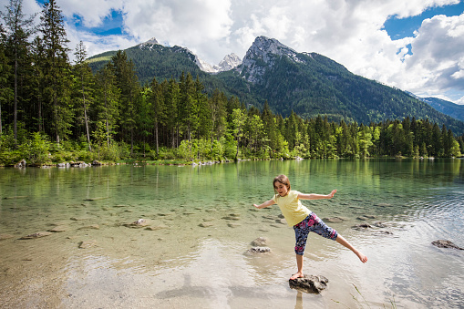 A girl with a yellow shirt stands in a mountain lake and enjoys playing. In the background stands the hochkalter mountain