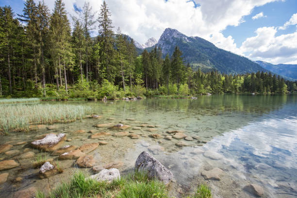 A girl with a yellow shirt stands in a mountain lake and enjoys playing. In the background stands the hochkalter mountain