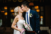 Portrait of an attractive bride who embraces the groom and holding bouquet of pink and purple flowers and greens with ribbon at the wedding ceremony.