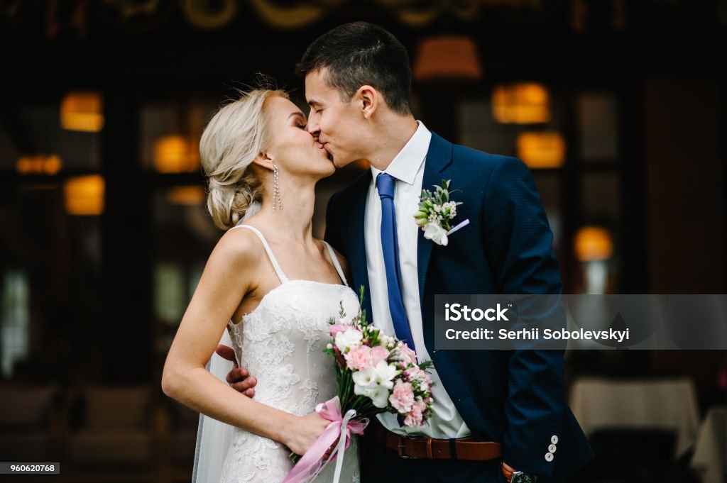 Portrait of an attractive bride who embraces the groom and holding bouquet of pink and purple flowers and greens with ribbon at the wedding ceremony. Wedding Stock Photo