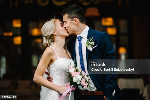 Portrait Of An Attractive Bride Who Embraces The Groom And Holding Bouquet Of Pink And Purple Flowers And Greens With Ribbon At The Wedding Ceremony Stock Photo - Download Image Now