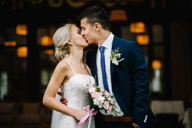 Photo of Portrait of an attractive bride who embraces the groom and holding bouquet of pink and purple flowers and greens with ribbon at the wedding ceremony.