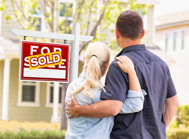 Caucasian Couple Facing Front of Sold Real Estate Sign and House Caucasian Couple Facing Front of Sold Real Estate Sign and House. sell home stock pictures, royalty-free photos & images