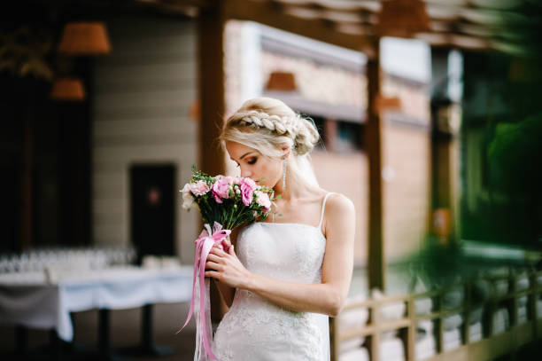 die junge schöne braut in einem eleganten kleid mit einem blumenstrauß steht im restaurant am ort für die trauung. - face paint audio stock-fotos und bilder