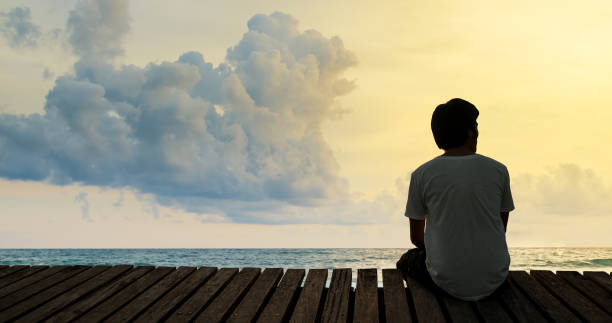 istock Silhouette alone young man relax siting on beach wooden walk way pier with sunset and cloud sky. Concept thinking and concentrate. Summer background copy space for label text banner or advertisement. 960631444
