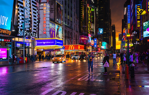 New York, USA - May 15, 2018: New York 42nd Street in colorful theatre Lights with orange Sunset Background, cars, tourists, reflecting the colorful sky juxtaposed with lit up LED display panels and signages.