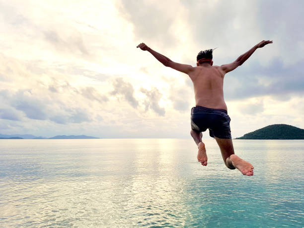 崖日没、夏の楽しいライフ スタイルで海に飛び込む - climbing men sea cliff ストックフォトと画像