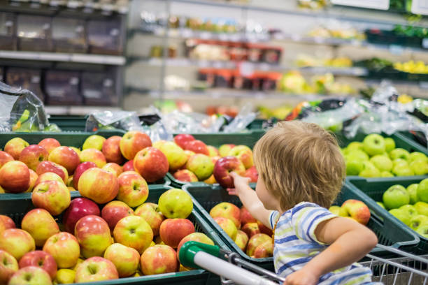 Small cute boy taking apple in supermarket
