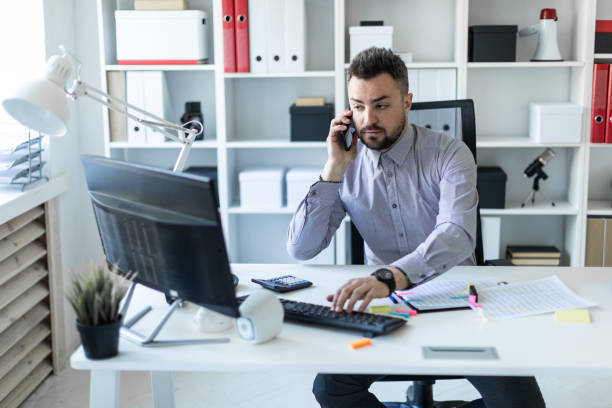 istock A young man is sitting in the office, talking on the phone and working on the computer. 960667296