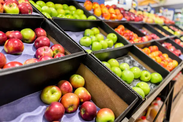 Many varieties assorted apples on display shelf in grocery store boxes in aisle, supermarket inside, nobody, including granny smith green and macintosh red fruit
