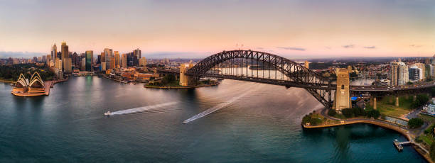 D Sy kirrib Pink Rise Major landmarks of Sydney city around Harbour on both sides of waterfronts connected by the Sydney Harbour bridge in wide aerial panorama at sunrise. sydney harbor photos stock pictures, royalty-free photos & images