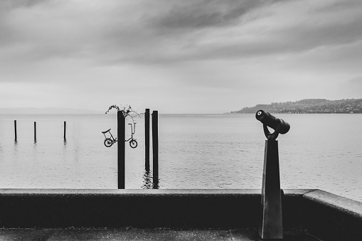 Black and white minimalist scene of a harbor with a coin-op viewer and several pillars with a bicycle in the pole