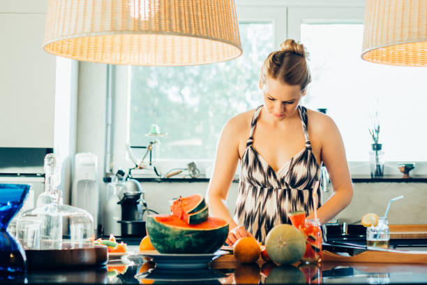 очаровательная женщина делает арбуз фруктовый салат на кухне - fruit salad fruit healthy eating making стоковые фото и изображения