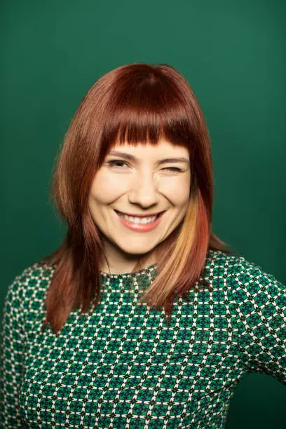 Portrait of woman winking over green background. Joyful female is with red hair. She is wearing casuals.