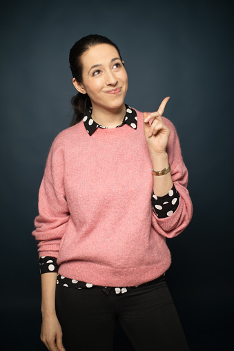 Thoughtful mid adult woman pointing upwards. Beautiful female is looking up while smiling. She is wearing casuals over colored background.