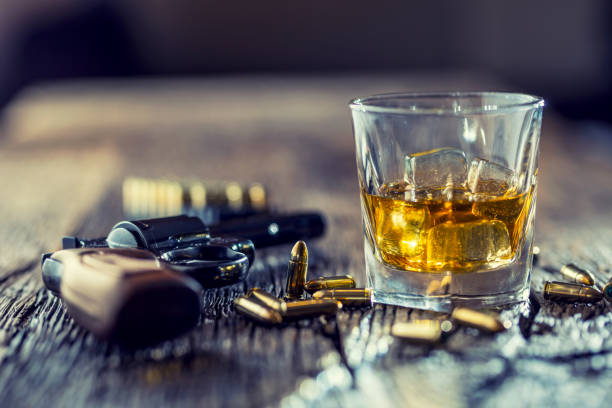 Glass of whiskey cognac or bourbon with revolver and bullets on wooden table Glass of whiskey cognac or bourbon with revolver and bullets on wooden table. gun mafia handgun bullet stock pictures, royalty-free photos & images