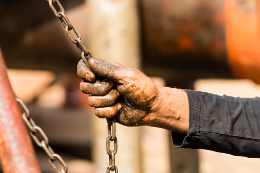 Worker at a shipyard in Dhaka Bangladesh holds a chain of a chain hoist with his oil-smeared hands