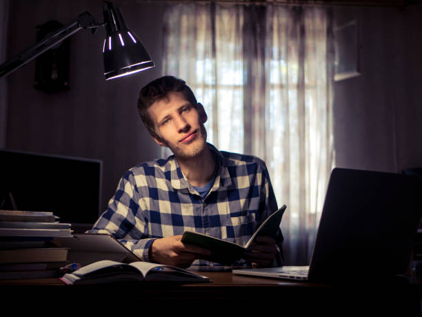 istock young bearded smiling student doing homework sitting at the table with lamp 960707242