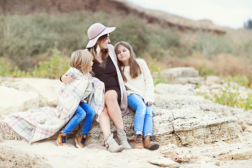 Fashionable pregnant woman in black dress and hat with daughters outdoors