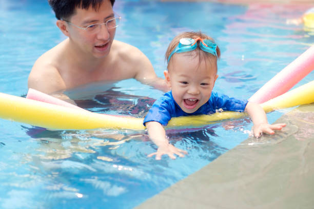 cute little asian 18 months / 1 year old toddler boy child wear swimming goggles learning to swim with pool noodle at outdoor pool - swimming child swimwear little boys imagens e fotografias de stock
