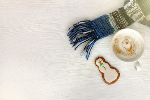 white mug with cappuccino in blue scarf and ginger snowman on table top view