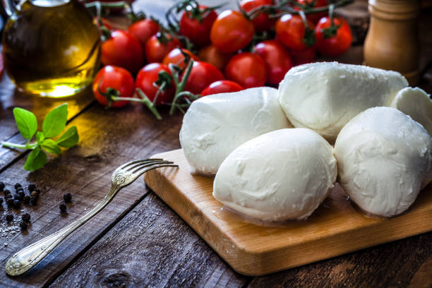 Mozzarella cheese Mozzarella cheese on a cutting board shot on rustic wooden table. On the table all around the board are ingredients for preparing Caprese salad like tomatoes, olive oil, basil, pepper and salt. Low key DSRL studio photo taken with Canon EOS 5D Mk II and Canon EF 100mm f/2.8L Macro IS USM mozzarella photos stock pictures, royalty-free photos & images