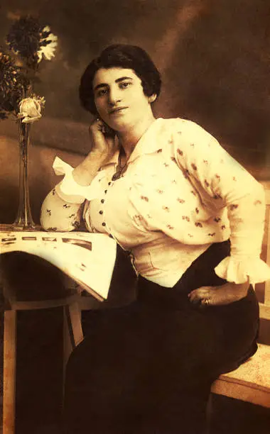 Vintage sepia toned photo  of a woman from the beginning of the twentieth century sitting at a desktop and reading a newspaper.