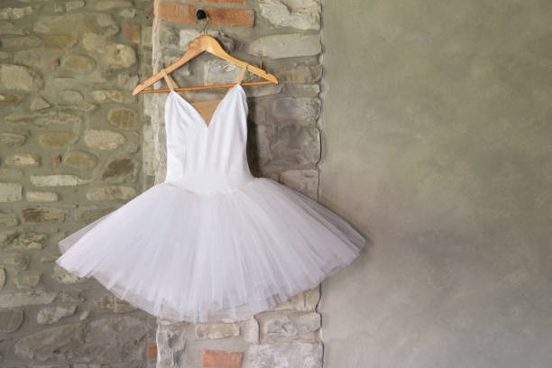 white classical ballet tutu hanging on wooden hanger, grey stone wall background