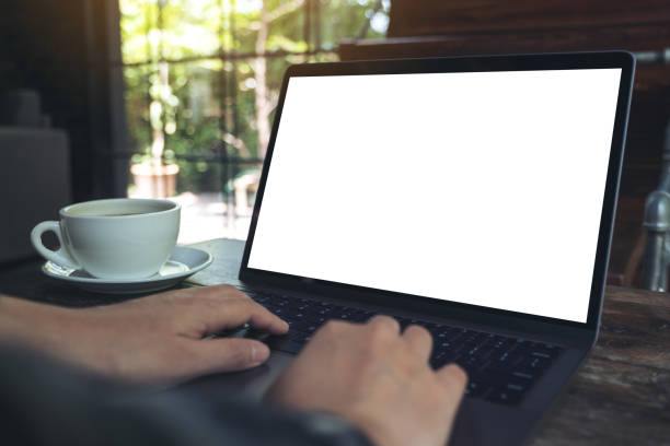 istock Mockup image of hand using laptop with blank white desktop screen with coffee cup on wooden table in cafe 960772882