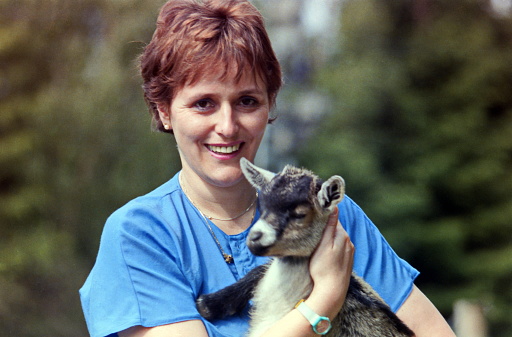 Bavaria, Germany at the eighties. A young red-haired woman hugs a baby goat.