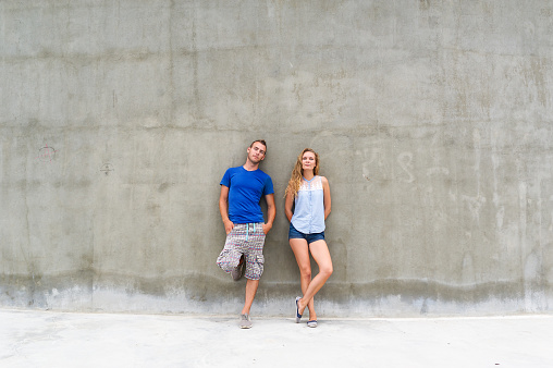 Portrait of beautiful young couple, looking at camera and smiling, standing against gray wall