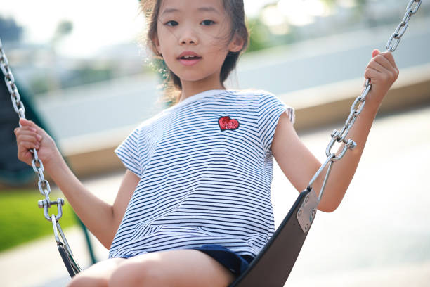 A pretty cheerful little girl is having fun on a swing in a playground.