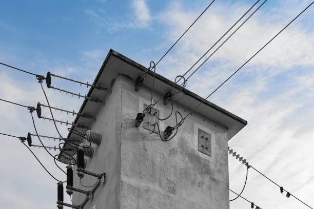 A abstract gray transformer house distributes the power lines against a blue cloudy sky