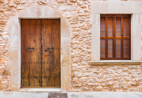 Close-up of brown wooden door and window shutters with rustic stone wall