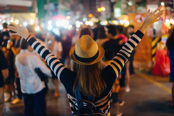 Photo of Young asian woman traveler backpacker with hat and bag traveling to Chiang Mai night walk street market at Chiang Mai Province, Thailand.