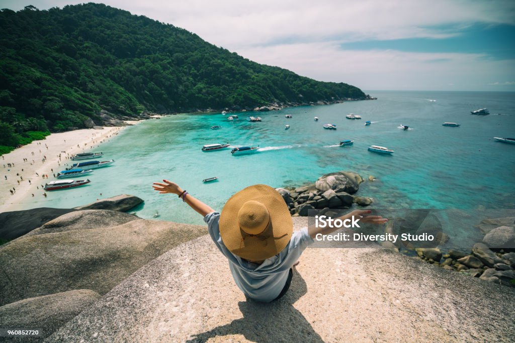 Summer concept Rear view of young woman traveler with hat sitting and relaxing on viewpoint at similan islands in Andaman sea at Phang Nga province near Phuket and Krabi in southern of Thailand. Summer Relax Phuket Island Stock Photo