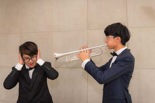 Portrait of young man playing trumpet to loudly sound and annoying his friend.