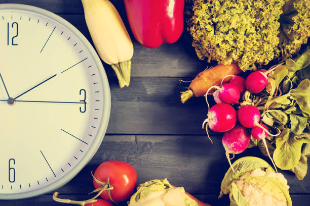 istock Clock and fresh vegetables. Zucchini, bell peppers, carrots, cabbage, cauliflower, radish, lettuce, tomato. Concept of a healthy diet. Copy space. 960872204