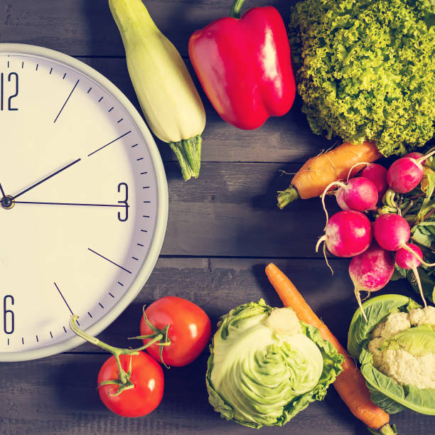 istock Clock and fresh vegetables. Zucchini, bell peppers, carrots, cabbage, cauliflower, radish, lettuce, tomato. Concept of a healthy diet. Copy space. 960872302