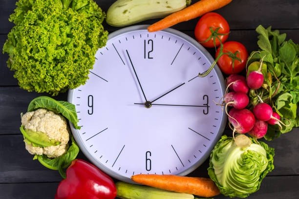 istock Clock and fresh vegetables. Zucchini, bell peppers, carrots, cabbage, cauliflower, radish, lettuce, tomato. Concept of a healthy diet. Copy space. 960875294