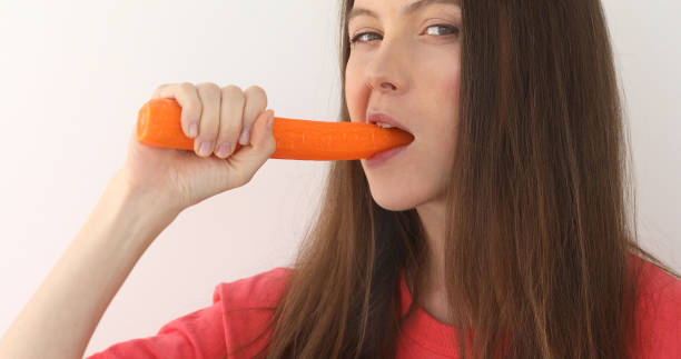 istock Smiling woman bites carrot studio portrait 960888460