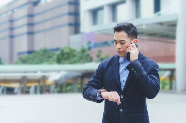 istock portrait attractive handsome business man using smartphone talking and looking smart watch at outdoor city with building background. technology connecting social online . 960894234