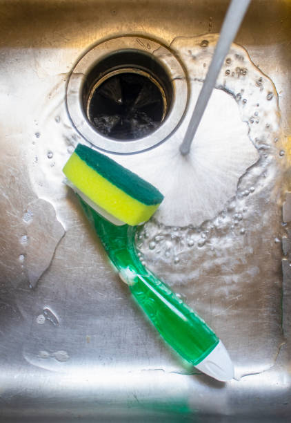 Water from tap running into stainless steel sink with pot scrubber lying in it. stock photo