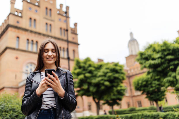 istock Single student walking and reading mobile phone messages with a university building in the background 960919236