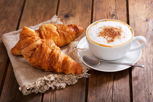 cup of cappuccino coffee with croissants on wooden table