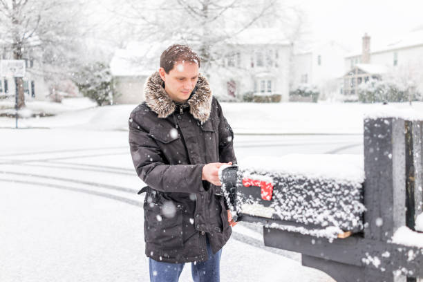 junger mann überprüfung post in nachbarschaft straße mit schnee bedeckten boden während blizzard weißen sturm, schneeflocken fallen in virginia vororten, einfamilienhäuser in postfach-box - mailbox mail us mail letter stock-fotos und bilder