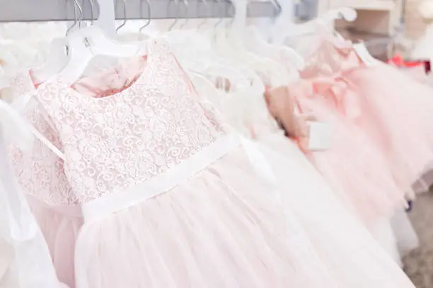 Many wedding flower girl party dresses in boutique discount store, pink garments hanging on rack hangers row closeup with white lace, tulle, design
