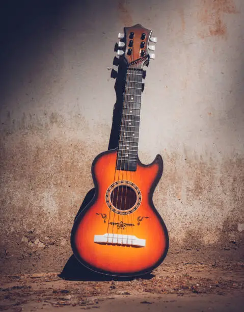 Wooden acoustic guitar outdoors in a street propped against the side of an old stone building on the sidewalk