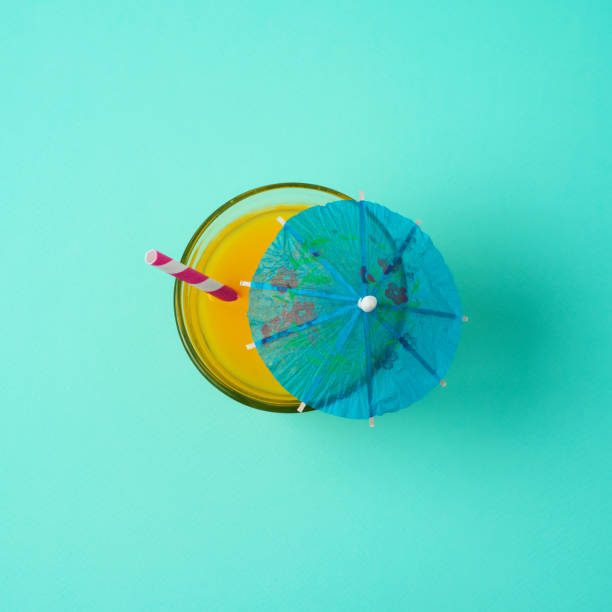 Minimal summer concept. Orange juice with umbrella and straw over blue background. View from above