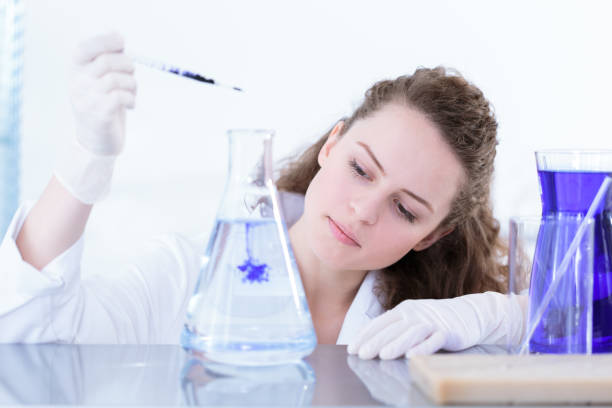 Chemist woman dropping violet oil Chemist woman dropping violet oil into solution while analysing product colloid stock pictures, royalty-free photos & images